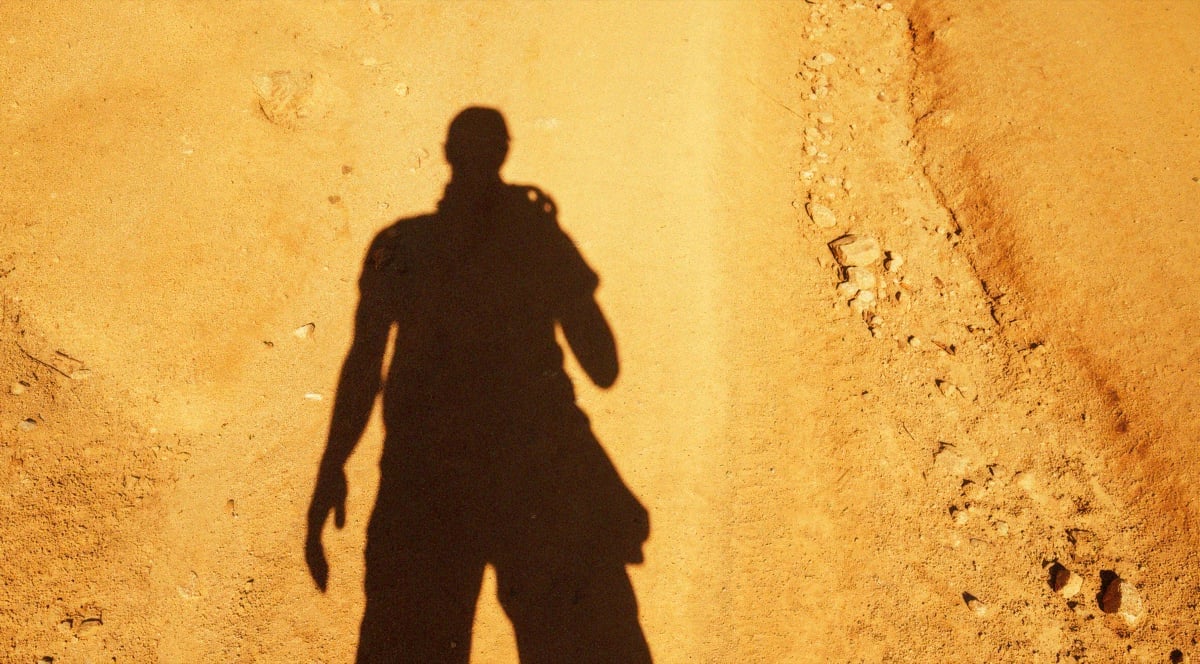 Shadow of a geologist cast across sunlit exploration ground